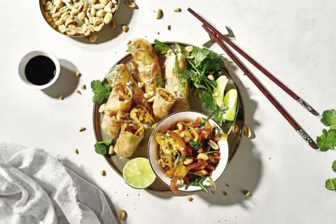 Frühlingsrollen mit Erdnüssen, Limette und Koriander – ein typisch asiatisches Essen, serviert mit Sojasauce und Stäbchen.