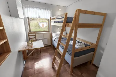 Enkel och mysig rum på vandrarhem Åre med våningssäng, litet bord och fönster med utsikt över grönskande landskap.