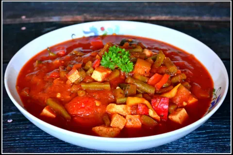 Pyszne leczo z tofu, z fasolką szparagową i papryką w sosie pomidorowym, udekorowane natką pietruszki.