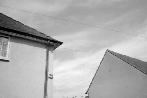 A black and white shot of two houses, captured on Kentmere 400 film. The image shows the roofs and walls of two buildings against a cloudy sky.