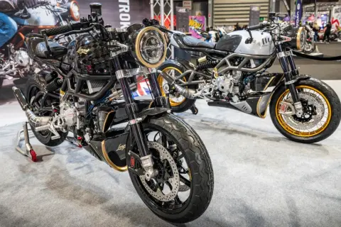 Dwa stylowe motocykle dwusuwowe, jeden czarny z elementami złota, drugi srebrny, prezentowane na wystawie.