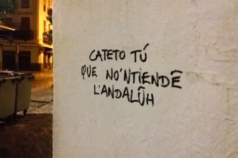 Graffiti en una pared con **expresiones sevillanas**: "Cateto tú que no'ntiende l'andalúh".