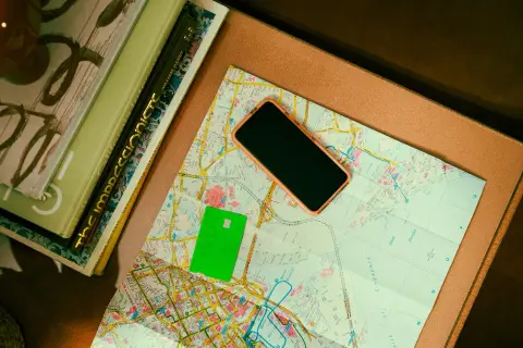 Zielona karta płatnicza, telefon i mapa leżą obok książek. Może to być przygotowanie do podróży, gdzie przyda się waluta Rumunii.