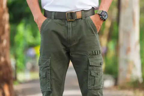 Uomo con outfit composto da pantaloni cargo verdi, cintura in tessuto e orologio sportivo.