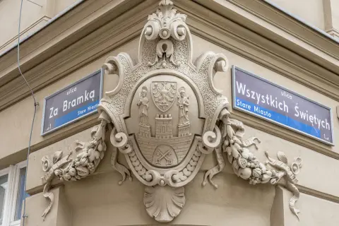 Bogaty herb zdobi fasadę kamienicy, obok tabliczek z nazwami ulic "Za Bramką" i "Wszystkich Świętych".