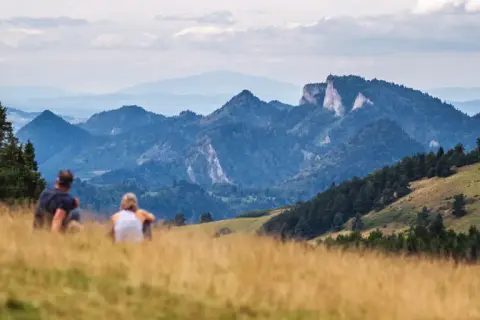 Para odpoczywa na trawiastym wzgórzu, podziwiając malownicze góry. To widok, który odpowiada na pytanie, gdzie leży Szczawnica.