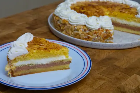 Un trozo de tarta o pastel de capas con crema y almendras, coronado con nata montada.