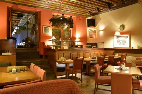 Przytulne wnętrze restauracji, gdzie zjeść w Krakowie na Rynku. Drewniane stoły, czerwone obicia i ciepłe oświetlenie tworzą atmosferę.