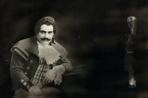 Ritratto di Enrico Caruso, la cui causa morte è ancora oggetto di dibattito. Indossa un costume d'epoca con baffi imponenti.