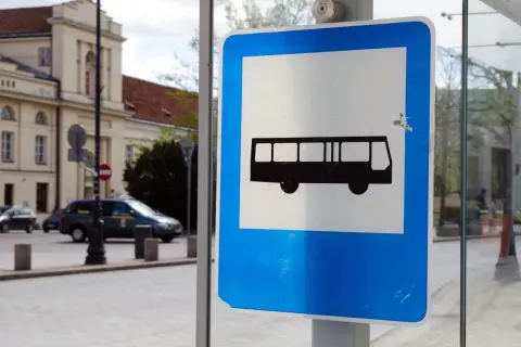 Znak przystanku autobusowego. Czy autobus ma pierwszeństwo? Na ulicy widać samochody i budynek.