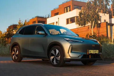Nowy Geely EX5 w kolorze zielonym, zaparkowany przed nowoczesnymi domami.