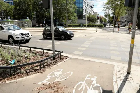 Czarny samochód wyprzedza na pasach, omijając białe auto. Na ścieżce rowerowej widoczne są symbole rowerów.
