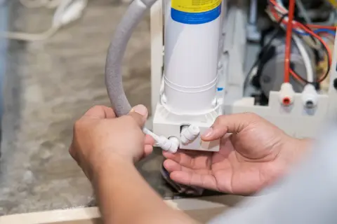 Mains d'un technicien connectant un tuyau à un adoucisseur d'eau, peut-être pour résoudre un problème d'eau salée.
