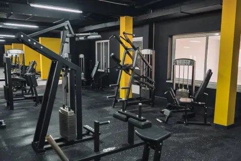 Gym med svarta väggar och gula pelare. Flera träningsmaskiner, inklusive en pec deck, står redo för ett träningspass.