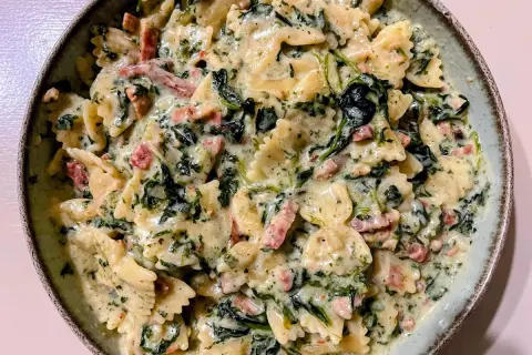 Pyszny makaron farfalle ze szpinakiem i kawałkami boczku w kremowym sosie.