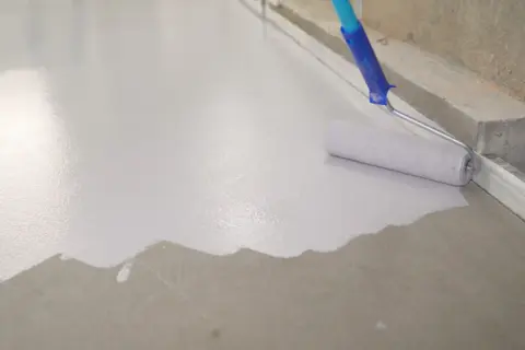 Wałek maluje beton na biało, tworząc gładką, jednolitą powierzchnię.