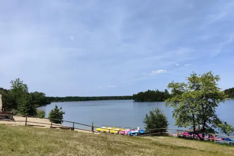 Słoneczny dzień nad jeziorem Chechło. Kolorowe rowerki wodne czekają na plaży, a w oddali widać zalesione brzegi.
