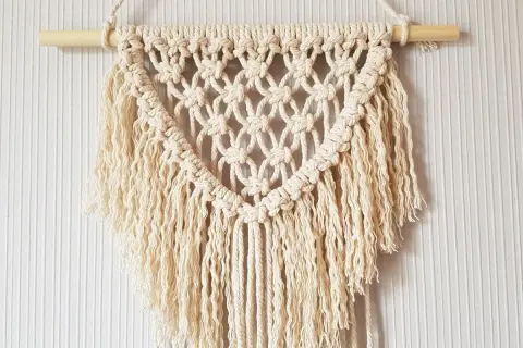 Un joli macramé tuto, suspendu à une tige de bois, avec des franges douces et un motif en losanges.