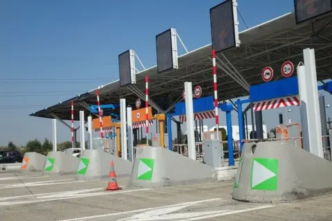 Voies de péage avec des indicateurs verts et orange. Une voie semble réservée au péage gratuit pour les handicapés.