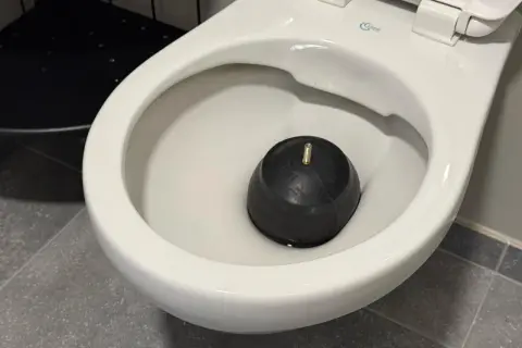 Un déboucheur en caoutchouc noir repose dans la cuvette d'un WC, prêt à résoudre les problèmes de diamètre d'évacuation WC.