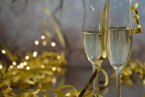 Dwa kieliszki szampana, złote serpentyny i migoczące światełka tworzą atmosferę noworocznych przesądów i celebracji.