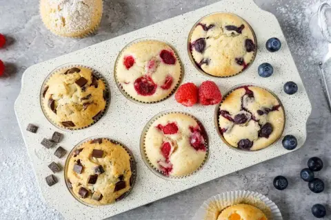 Leckeres mini muffins rezept: Schoko-, Himbeer- und Blaubeermuffins in einer Muffinform, garniert mit frischen Beeren und Puderzucker.