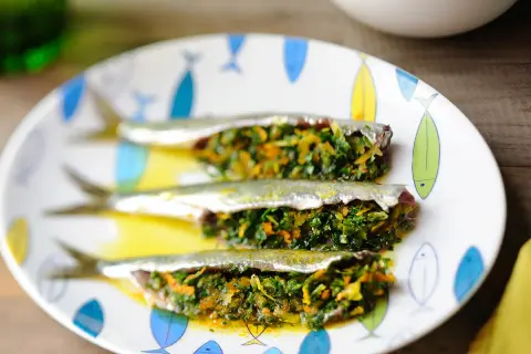 Trois sardines farcies aux herbes et légumes, servies sur une assiette décorée de poissons.
