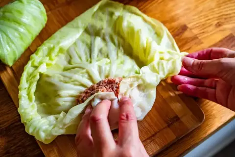 Ręce zwijają gołąbki z farszem mięsnym w liście kapusty. Idealny przepis na gołąbki na 1kg mięsa.