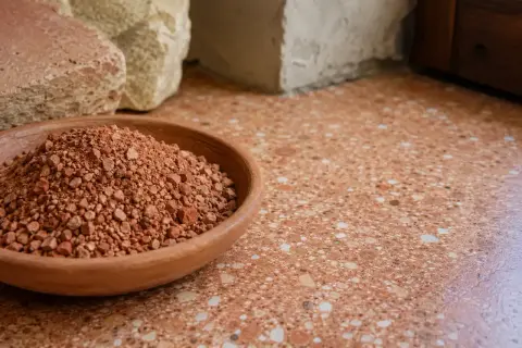 Ciotola di terra rossa, materiale grezzo per il rinzaffo significato. Sotto blocchi di pietra e un pavimento in graniglia.