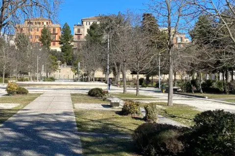 Passeggiata invernale nei giardini Diaz a Macerata, con alberi spogli e palazzi sullo sfondo.