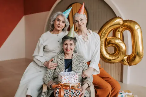 Eleganckie stylizacje na urodziny w lokalu. Trzy kobiety świętują 60. urodziny, otoczone prezentami i złotymi balonami.