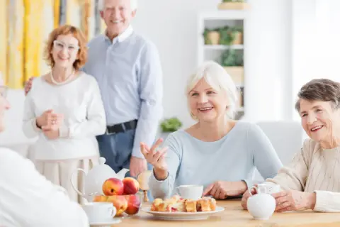 Des aînés souriants partagent un moment convivial autour d'un thé et de pâtisseries. Une définition de la marpa : un lieu de vie chaleureux pour seniors.