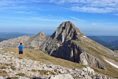 Un randonneur admire la majesté de la grande moucherolle, un pic rocheux imposant sous un ciel bleu.