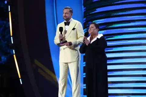 Mężczyzna w żółtym garniturze i kobieta w czarnej sukni na scenie, trzymają mikrofony. To szczyt możliwości, top of the top!