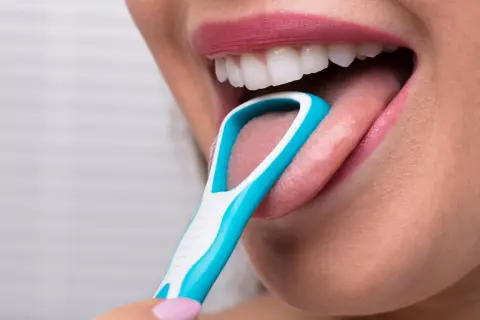 Una persona usa un puliscilingua azzurro per pulire la lingua, un gesto che ricorda la lava lingua.