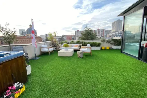 Terraza con césped artificial verde, jacuzzi, muebles de exterior y vistas urbanas. Ideal para aprender como limpiar césped artificial terraza.