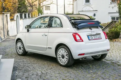 Biały fiat 500c cabrio z otwartym dachem stoi na brukowanej uliczce.