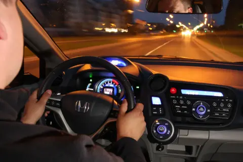 Kierowca prowadzi auto nocą. Czy w czasie jazdy w nocy masz obowiązek zwiększyć uwagę? Widok z wnętrza pojazdu na drogę i deski rozdzielcze.