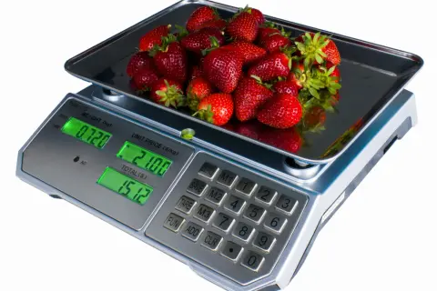 Kobiałka pełna soczystych truskawek waży się na wadze cyfrowej, pokazując 0.720 kg.