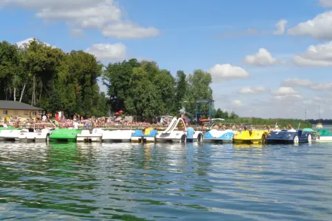 Słoneczny dzień nad jeziorem w Powidzu. Rząd kolorowych rowerów wodnych czeka na plażowiczów.