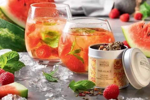 Deux verres de thé glacé maison aux fruits rouges et menthe, accompagnés de pastèque, framboises et d'une boîte de thé.