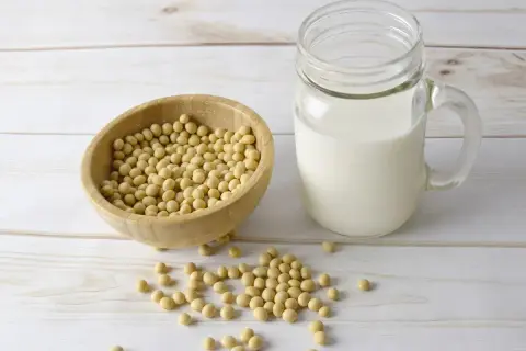Bol en bois rempli de graines de soja à côté d'un verre de lait de soja. Découvrez les lécithine de soja bienfaits pour votre santé.