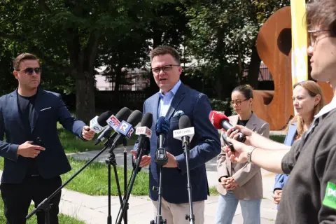 Wpływ social mediów i podcastów na popularność Polska 2050: polityk przemawia do mediów, otoczony mikrofonami.