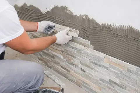 Pose de pierre de parement sur un mur avec du mortier. Un artisan pose méticuleusement les pierres pour un revêtement mural naturel.