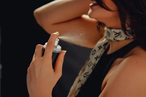 Kobieta rozpyla mgiełkę perfum na szyję.