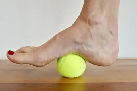 Fuß auf einem Tennisball zur achillessehne dehnen. Sanfter Druck auf die Ferse zur Lockerung.