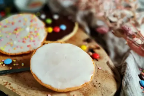 Bunte Kekse mit Zuckerguss und Schokoladenglasur, inspiriert von einem amerikanischen Rezept, liegen auf einem Holzbrett.