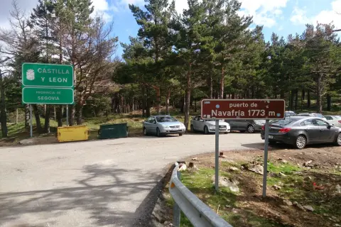 Señal de "puerto de Navafría 1773 m" junto a señales de Castilla y León y Segovia. Coches aparcados en un día soleado.