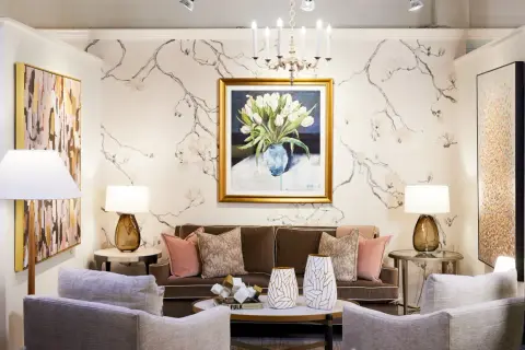 A living room with traditional interior design, featuring a floral wallpaper, a painting of tulips, a brown sofa, and plush armchairs.