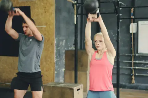 Uomo e donna eseguono esercizi con kettlebell, un allenamento completo per diversi gruppi muscolari in palestra.